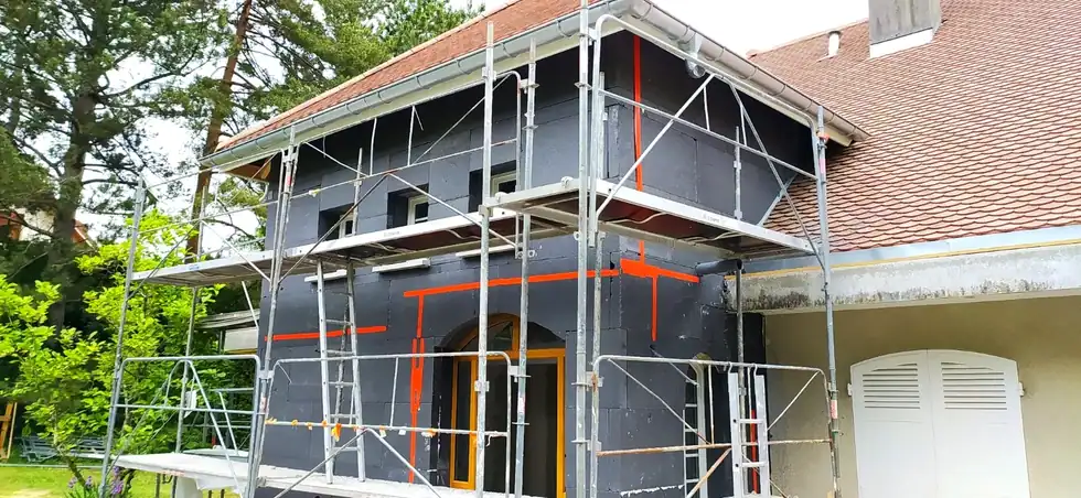 Façade de maison en travaux avec échafaudage et bandes orange de préparation