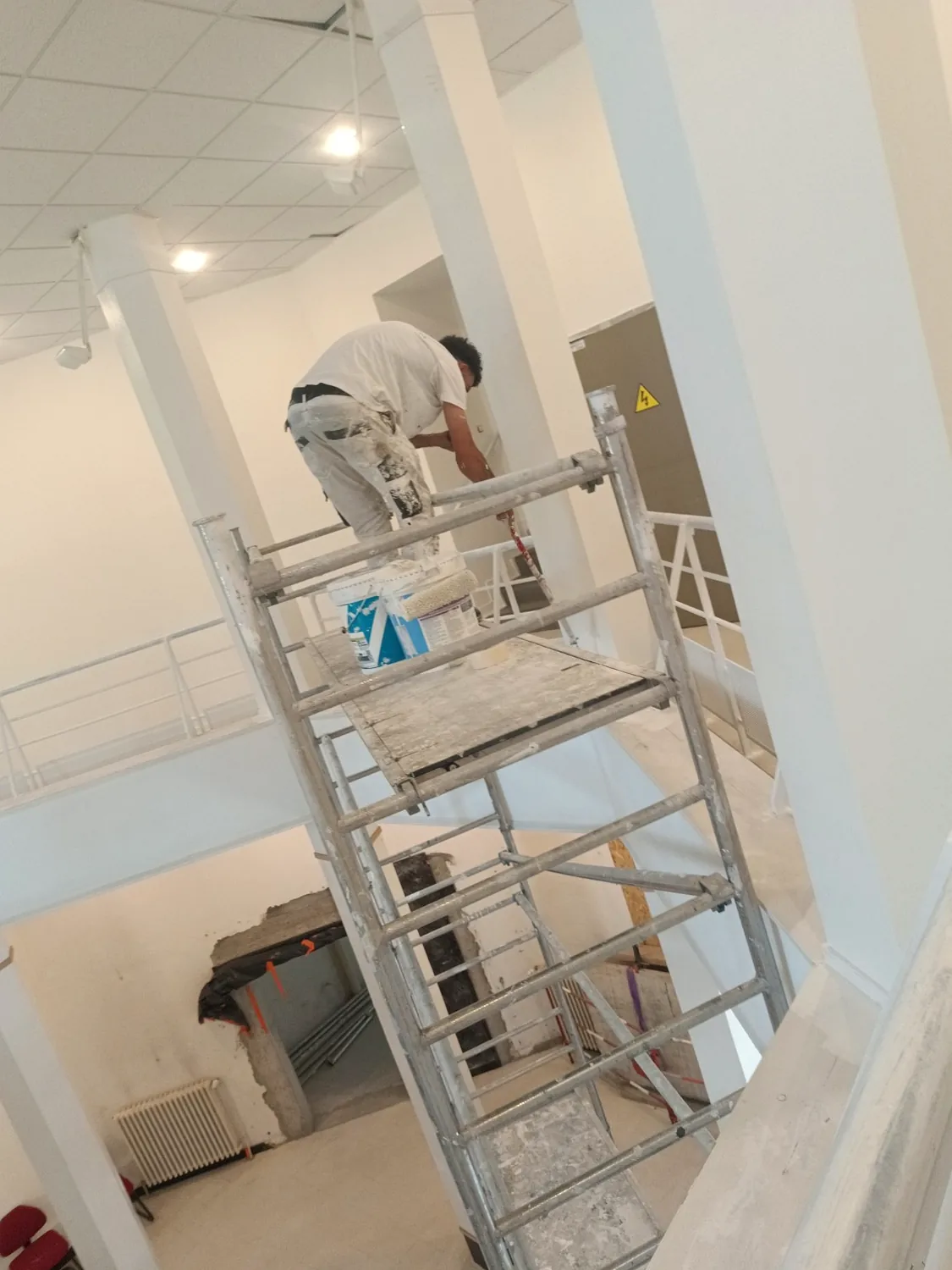 Peintre sur échafaudage roulant dans un grand espace intérieur